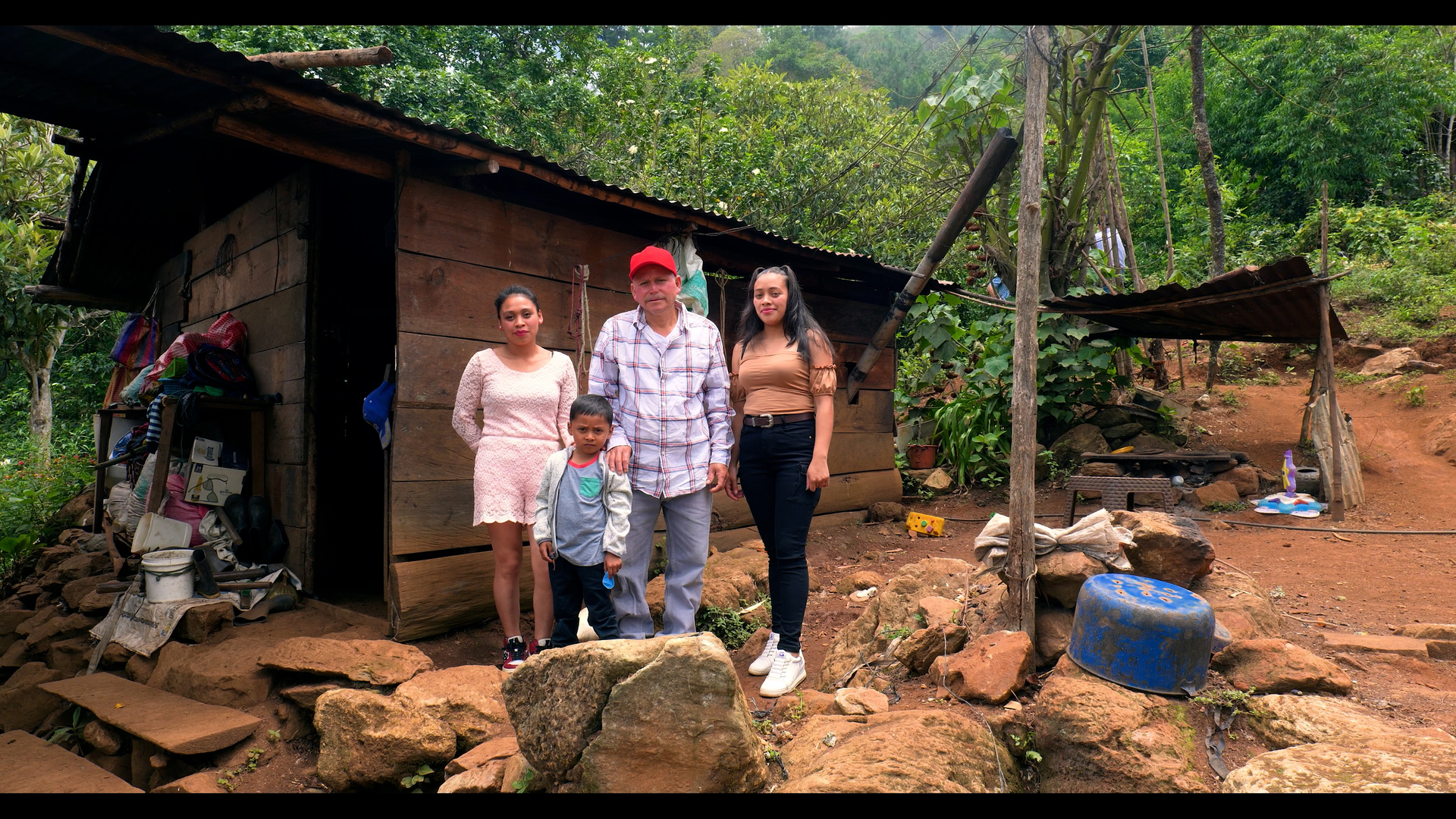 Familia guatemalteca frente a su vivienda de madera con piso de tierra